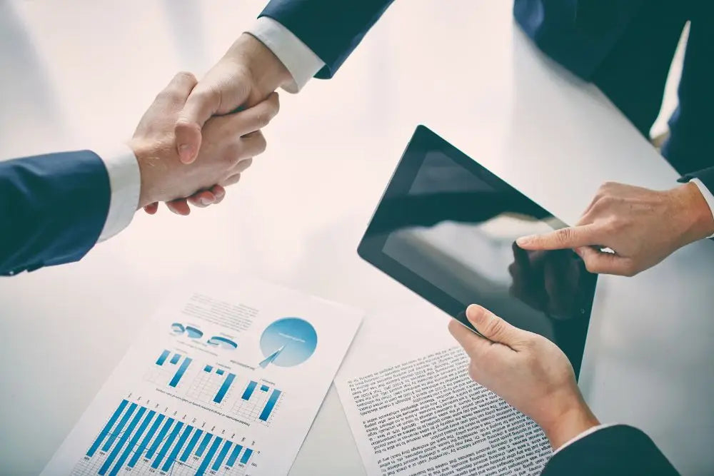 Handshake in business attire with tablet and financial documents in Dirextra alta formazione.